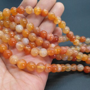 May include: A strand of carnelian beads, featuring a mix of orange and red tones. The beads are round and smooth, with a natural, polished finish.