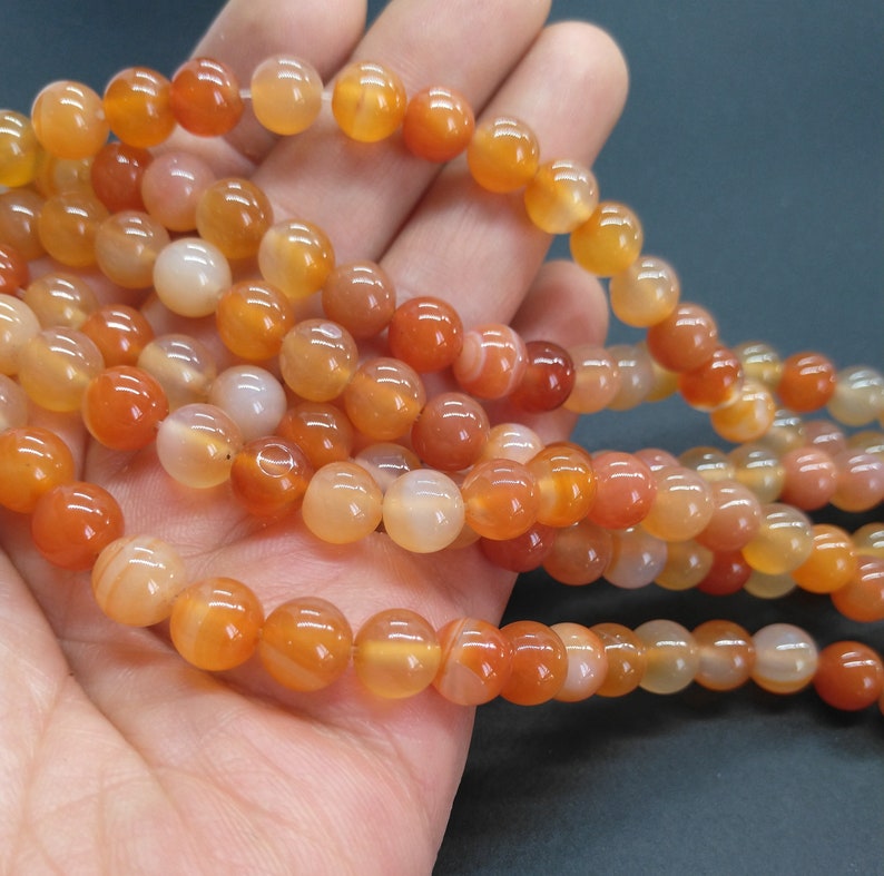 May include: A strand of carnelian beads, featuring a mix of orange and red tones. The beads are round and smooth, with a natural, polished finish.