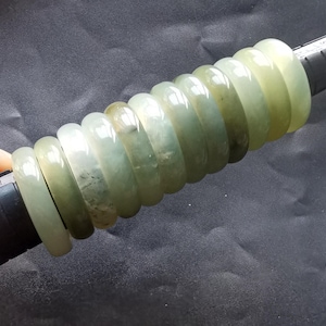 Può includere: Un mucchio di braccialetti di giada in varie tonalità di verde. I braccialetti sono lisci e lucidi, con un leggero bagliore.