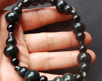 Puede incluir: Pulsera de jade verde oscuro con una serie de cuentas en forma de calabaza y cuentas redondas más pequeñas. La pulsera está ensartada, creando un diseño único y orgánico. El jade tiene un acabado pulido y brillante.