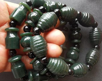 May include: Dark green jade bracelets with a mix of barrel and vase-shaped beads, strung together with small black beads. The bracelets are displayed in a hand, showcasing the polished finish and color variations of the jade.
