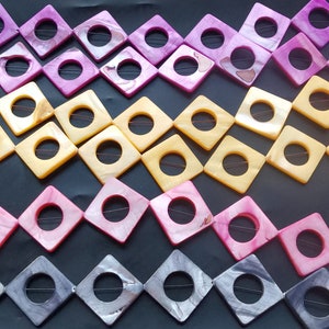 May include: A strand of square-shaped shell beads with a hole in the centre. The beads are in four colours: pink, yellow, light pink, and grey.