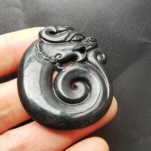 May include: A black jade pendant carved in the shape of a dragon with a swirling tail. The pendant is smooth and polished.