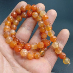May include: A strand of orange carnelian beads, each bead is round and smooth. The beads are strung on a clear thread.
