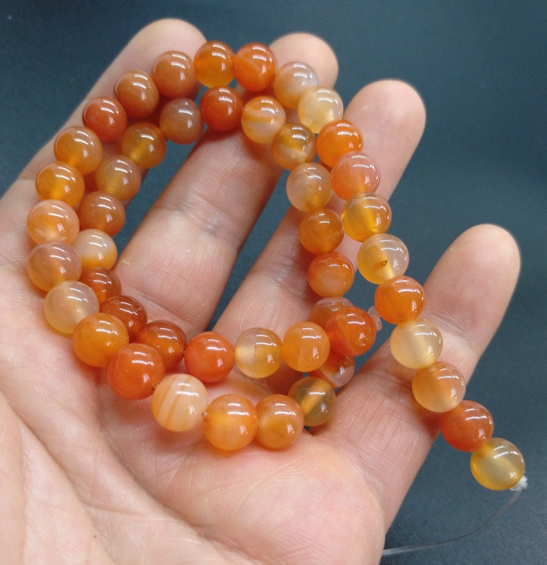 May include: A strand of orange carnelian beads, each bead is round and smooth. The beads are strung on a clear thread.
