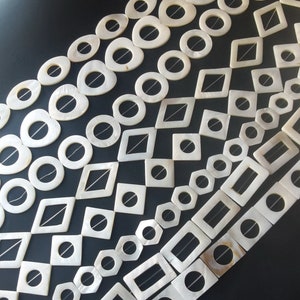 Può includere: Una collezione di perline bianche di madreperla in varie forme, tra cui cerchi, quadrati ed esagoni. Le perline hanno un foro al centro e sono infilate su un filo sottile.