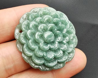 May include: A green jade pendant carved in the shape of a flower. The flower has many layers of petals and a center with a small hole.