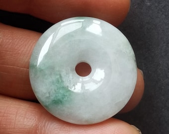 May include: A round, polished jade pendant with a central hole. The pendant is primarily white with areas of light green marbling. The surface is smooth and reflective, suggesting a high-quality finish. The jade is held between fingers.