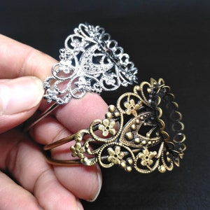 May include: Two ornate metal bracelets, one silver and one gold, with intricate floral designs. The bracelets are stacked on top of each other.
