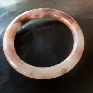 Puede incluir: Un brazalete redondo y pulido con tonos rosas y marrones. El brazalete está hecho de un material liso y translúcido, con variaciones de color. Un accesorio sencillo y elegante.