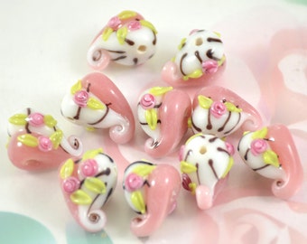 May include: A collection of ten pink and white glass beads with floral and swirl designs. The beads are approximately 2.5 cm in length and have a hole for stringing.