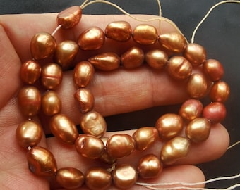 May include: A strand of brown freshwater pearls with a slightly iridescent sheen. The pearls are strung on a white thread and are approximately 8mm in diameter.