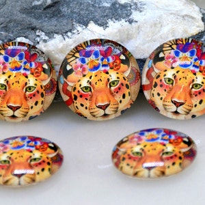 Puede incluir: Cinco cabujones de vidrio redondos y ovalados con una imagen colorida de un leopardo con una corona de flores. El leopardo tiene un pelaje naranja con manchas negras y ojos verdes.