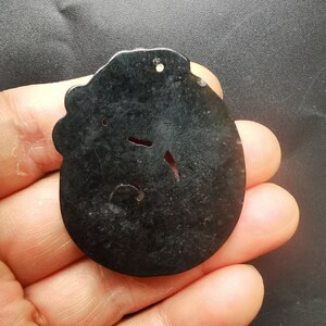 May include: A black jade pendant with a carved design. The pendant has a hole at the top for a cord or chain.