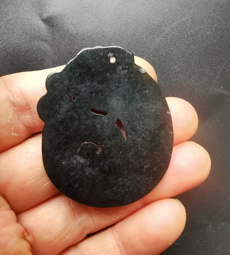 May include: A black jade pendant with a carved design. The pendant has a hole at the top for a cord or chain.