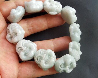 Op de afbeelding: Een jade armband met gegraveerde lachende gezichten. De armband is gemaakt van lichtgroene jade en heeft een gepolijste afwerking.
