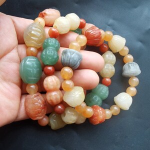 May include: A multi-strand bracelet made of jade beads in various colors, including green, orange, and red. The beads are carved into different shapes, including gourds, flowers, and round beads.