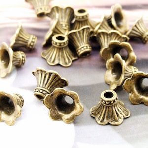 May include: A collection of antique gold-toned metal flower-shaped bead caps. The caps have a decorative design and a hole in the center for stringing.