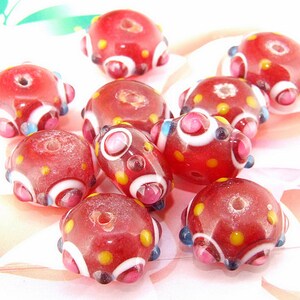 Peut inclure: Dix perles en verre rouge avec des accents blancs, jaunes et bleus. Les perles ont une surface texturée mouchetée et sont rondes avec un trou au centre.