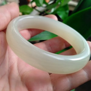 Puede incluir: Un brazalete de jade blanco. El brazalete es liso y pulido, con un ligero brillo.