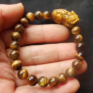 May include: A brown tiger's eye beaded bracelet with a carved tiger head charm. The beads are round and have a golden sheen.