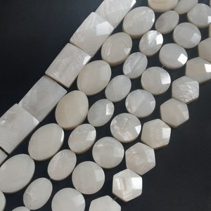 May include: A collection of white mother of pearl beads in various shapes and sizes. The beads are arranged in rows, with the largest beads at the top and the smallest beads at the bottom. The beads have a smooth, polished surface and a subtle iridescent sheen.