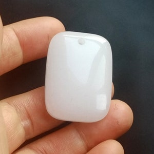 Könnte beinhalten: Ein weißer, glatter, rechteckiger Anhänger mit einem kleinen Loch oben.