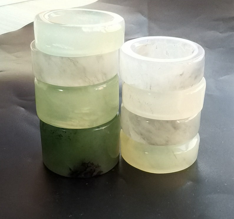 May include: A stack of five white jade rings, with a stack of four green jade rings next to them. The rings are smooth and polished, and they have a natural, organic look.