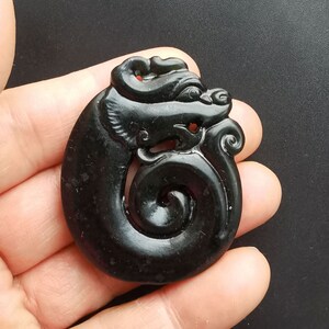 May include: A black jade pendant carved in the shape of a dragon. The dragon is curled around a spiral, and its head is facing to the right. The pendant is smooth and polished.