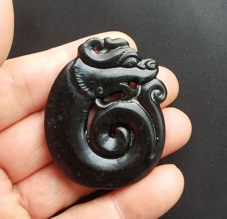 May include: A black jade pendant carved in the shape of a dragon. The dragon is curled around a spiral, and its head is facing to the right. The pendant is smooth and polished.