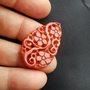 May include: A red carved pendant with a floral design. The pendant is made of a smooth, polished stone.