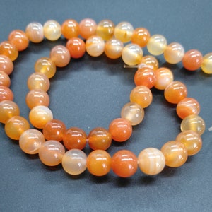May include: A strand of carnelian beads in shades of orange and red. The beads are round and smooth, and they are strung on a clear elastic cord.