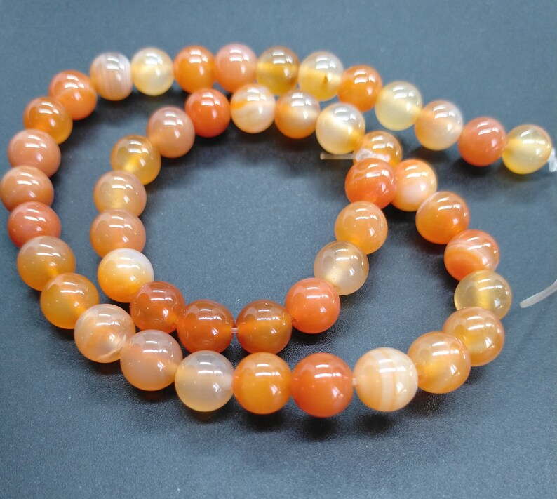 May include: A strand of carnelian beads in shades of orange and red. The beads are round and smooth, and they are strung on a clear elastic cord.