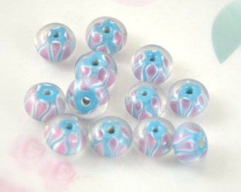 May include: A collection of 12 round, clear glass beads with a blue and pink swirl pattern. The beads have a hole in the centre for stringing.