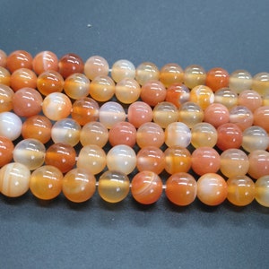 May include: A strand of carnelian beads, featuring a mix of orange and white tones. The beads are round and smooth, with a polished finish.