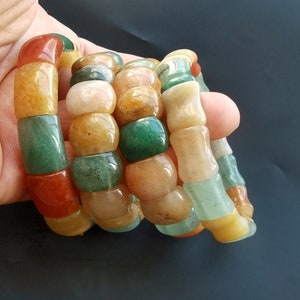 Op de afbeelding: Vier gestapelde armbanden gemaakt van kleurrijke edelsteen kralen. De armbanden zijn gemaakt van groene, oranje en bruine kralen.