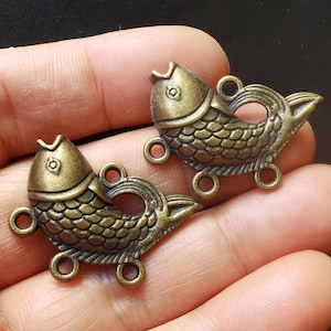 May include: Two antique gold-toned fish charms with detailed scales and open rings for attaching to jewelry or crafts.