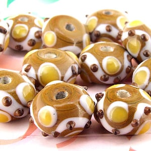 May include: A collection of brown, white and yellow glass beads with a speckled pattern. The beads have a hole in the centre and are designed for jewellery making.