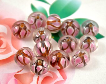 May include: A collection of round, clear glass beads with pink and brown floral patterns. The beads are translucent and have a glossy finish.