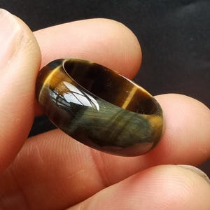May include: A brown and gold tiger's eye gemstone ring. The ring is polished and has a smooth, rounded surface.