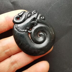May include: A black jade pendant carved in the shape of a dragon with a swirling tail. The pendant is intricately detailed and has a glossy finish.