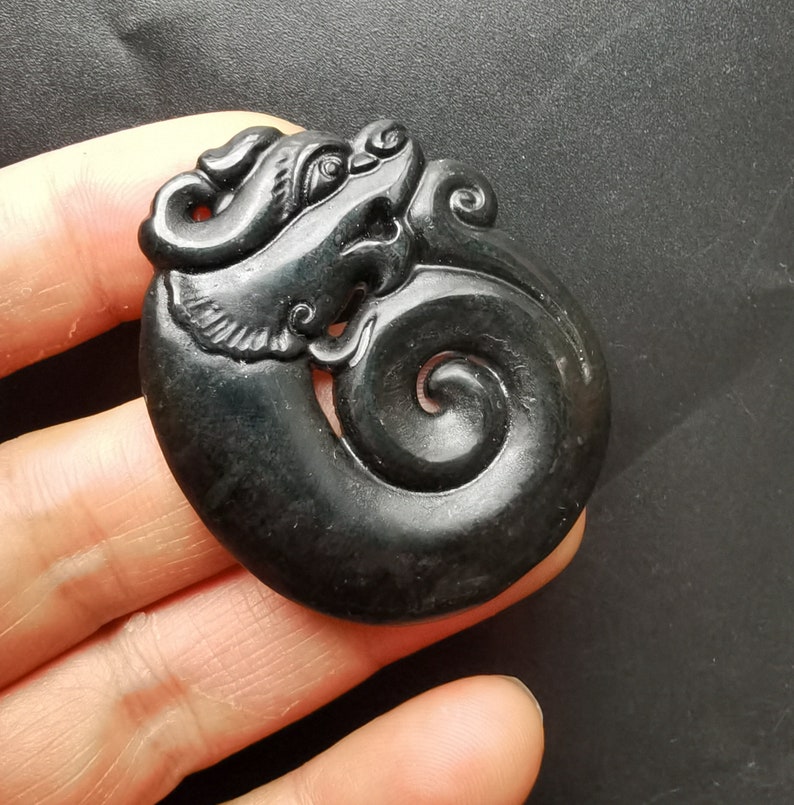 May include: A black jade pendant carved in the shape of a dragon with a swirling tail. The pendant is intricately detailed and has a glossy finish.