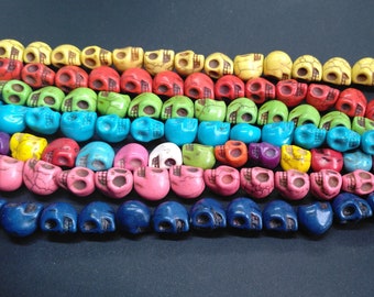 Puede incluir: Un surtido colorido de cuentas en forma de calavera hechas de piedra turquesa. Las cuentas están dispuestas en filas, cada fila con un color diferente. Los colores incluyen azul, verde, rosa, rojo, amarillo y blanco.