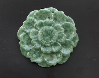 May include: A green jade flower pendant carved in a detailed floral design. The pendant is a light green color with a slightly translucent quality.