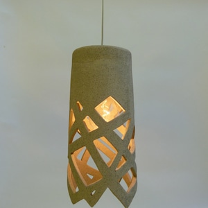 May include: A beige ceramic pendant light with a geometric cut-out design. The light is on and illuminates the room.