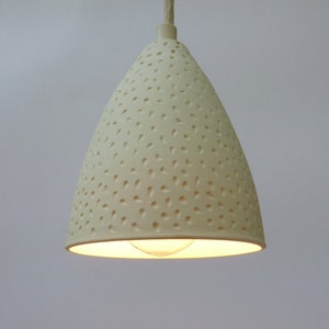 Peut inclure: Un luminaire suspendu en céramique blanche avec un abat-jour conique. L'abat-jour a une surface texturée avec de petits trous espacés uniformément.