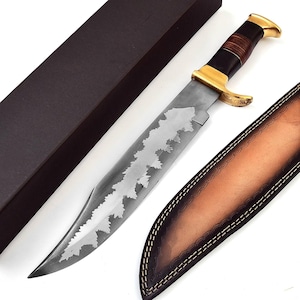 May include: A large, silver-bladed knife with a decorative etched design, a dark brown handle, and gold accents. The knife is accompanied by a brown leather sheath and a black box, suggesting a presentation or storage case.