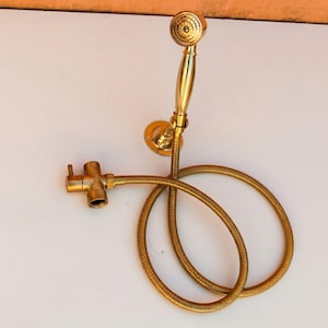 May include: A vintage-style, gold-colored shower head and hose set. The showerhead has a round, patterned design, and the hose is coiled. The set includes a wall mount and a valve. The overall design is ornate and classic.