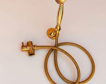 May include: A gold-coloured shower head and hose set in a vintage style. The showerhead features a round, patterned design, and the hose is coiled. The set includes a wall mount and a valve. The overall design is ornate and classic.