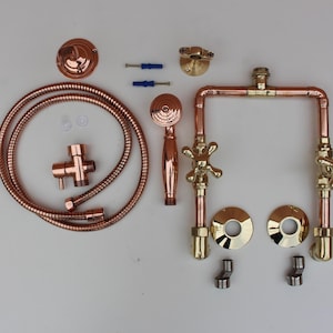 May include: A copper shower system kit including a flexible hose, a handheld shower head, a wall-mounted bracket, two cross-handle valves, two circular escutcheon plates, two threaded connectors, and two blue wall anchors for installation.